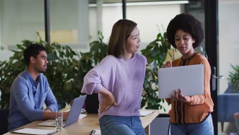 Diverse-business-people-talking-using-a-laptop-in-modern-office