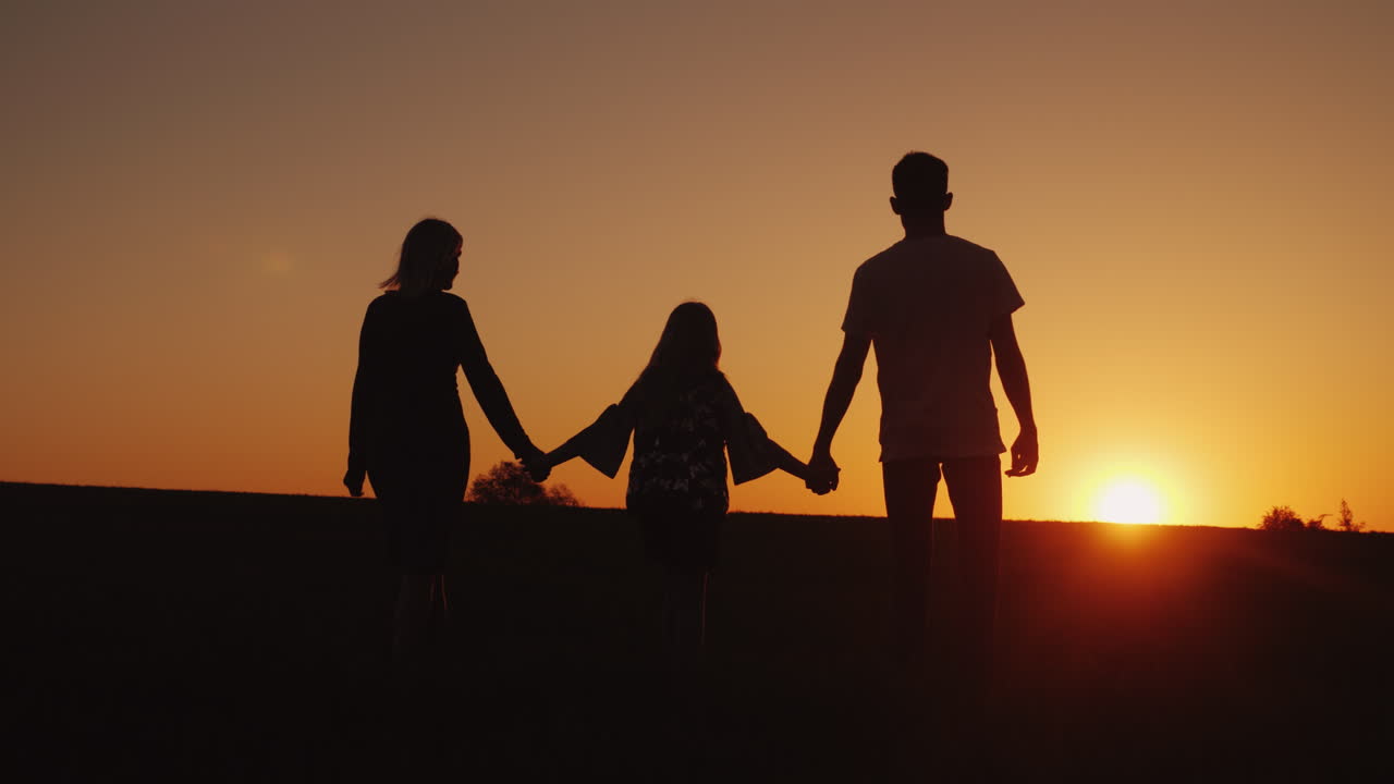 Genitori con il bambino avanzano verso il tramonto. Silhouette familiari.