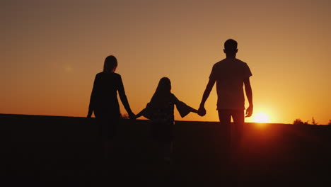 parents with the child go forward towards the sunset family silhouettes