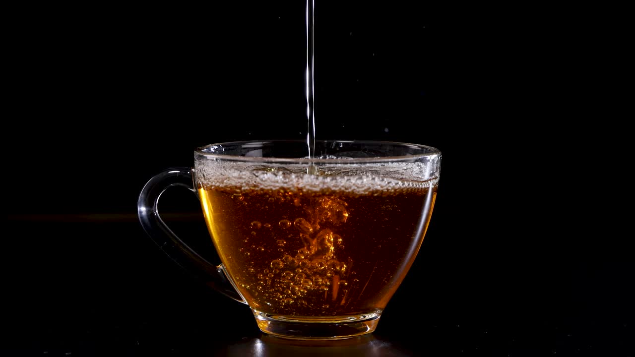 A sequence of tea being poured into a transparent glass cup against a dark backdrop, highlighting the liquid's rich color