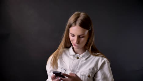 una joven genial está viendo fotos en su teléfono inteligente, se conmueve, concepto de comunicación, fondo gris