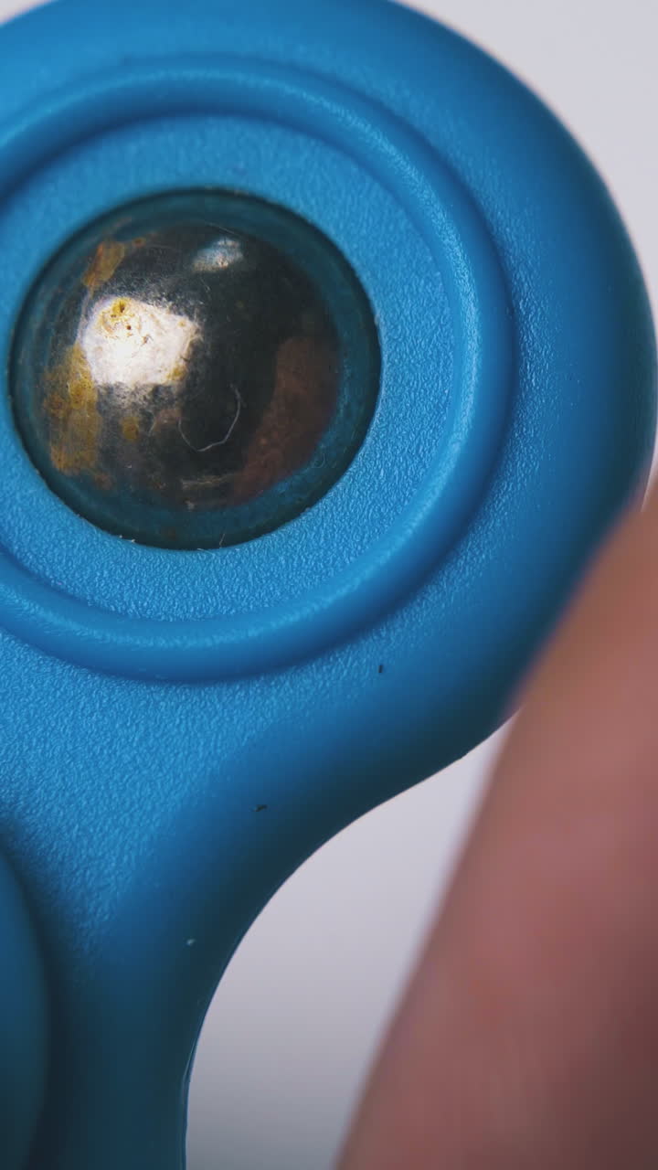 young man have fun playing with blue spinner with shiny metal ball on light background extreme close view