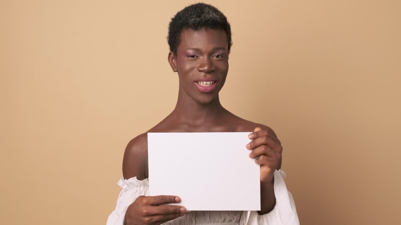 African transgender person smiling while holding a white blank paper sheet.