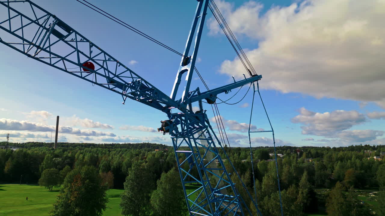 Rear strut and front strut of a blue luffing construction crane against a blue sky and clouds with forest in background