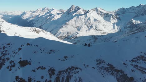 Aerial-view-over-free-ride-skiers,-getting-ready-to-freestyle-from-the-mountain-summit---reverse,-drone-shot