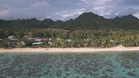 sunlight glows and shines on coastline of sandy beach and mountains above fringing reef protecting waters in rarotonga cook islands
