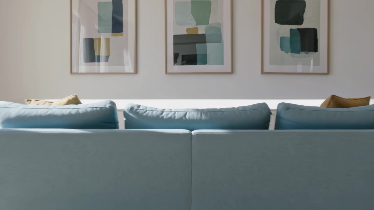 Moving camera approaching teal three-seat sofa in model apartment, showing framed art and LED shelf