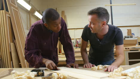 carpenter with apprentice sanding wood in workshop