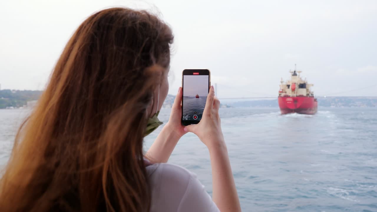 una mujer turista toma una foto de un barco de carga que navega en el estrecho del bósforo