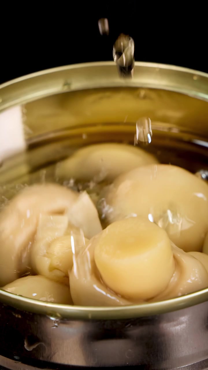 Una vista ravvicinata di una lattina di metallo piena di funghi champignon in liquido, che cattura una goccia d'acqua che schizza e crea bolle sotto una luminosa illuminazione da studio.