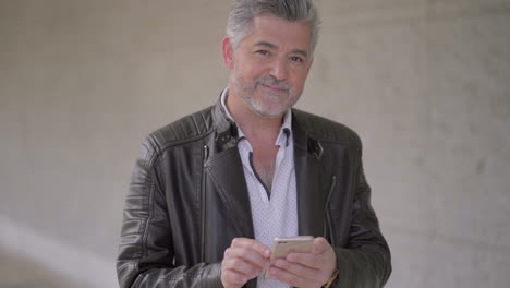 Mature-man-using-smartphone-and-smiling-at-camera