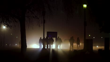 People-waking-on-a-dark-street-with-car-back-lighting-them,-rainy-day,-glow,-haze,-fog,-Niagara-Falls,-Canada