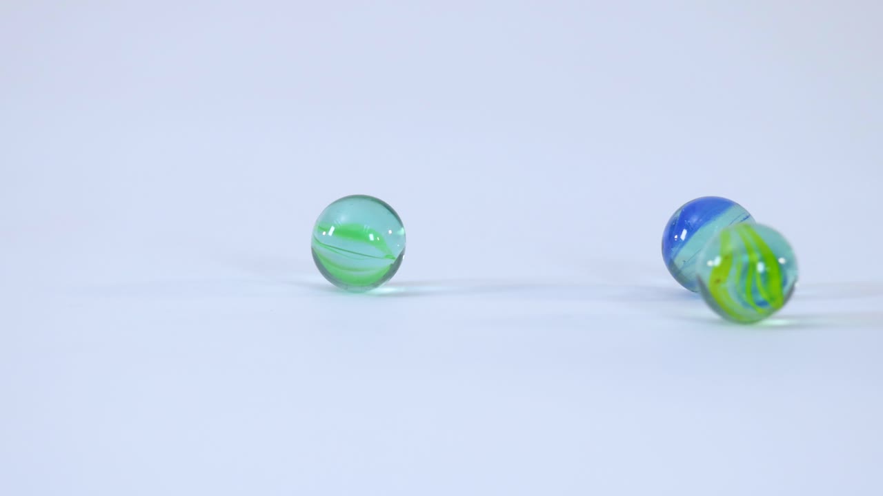 Clear glass marbles with colorful swirls roll and bounce across a bright white studio background