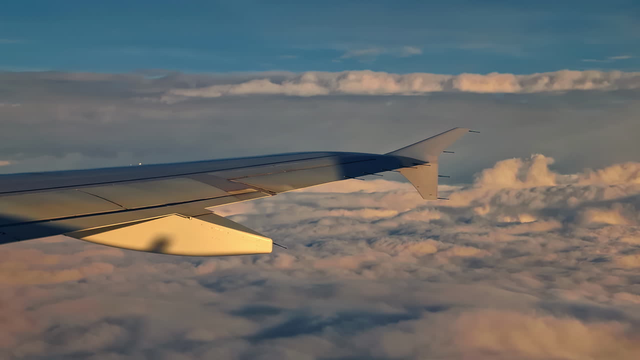 Airplane wing on a commercial jet flying over clouds at sunset