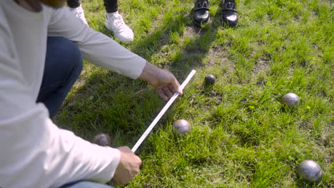 bovenaanzicht van een man die de afstand tussen petanqueballen in het park berekent