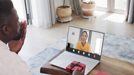 African-american-man-holding-gift-and-talking-with-biracial-woman-on-laptop-screen