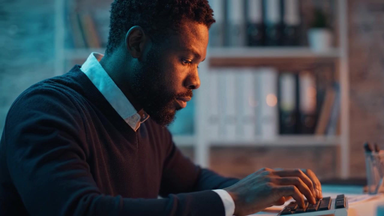 Focused individual engaged in typing on a keyboard under soft lighting, showcasing a moment of concentration and creativity in a serene workspace environment.