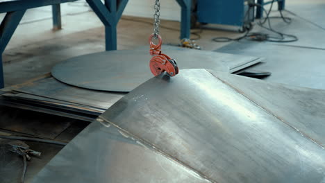 sheets of metal on the floor in a warehouse. the crane hook lifts the metal part. slow motion
