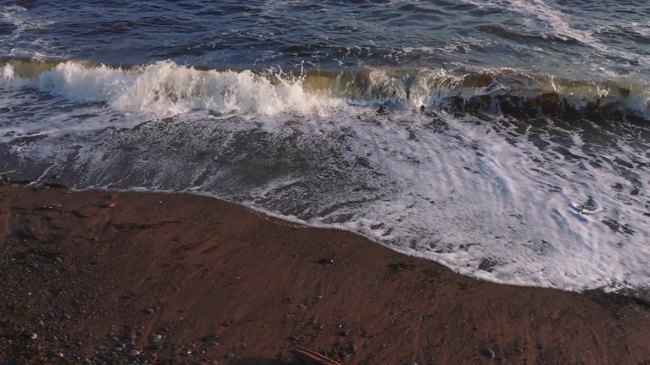 Lenta ripresa aerea che orbita intorno a una spiaggia di sabbia rossa mentre le onde si infrangono sulla riva