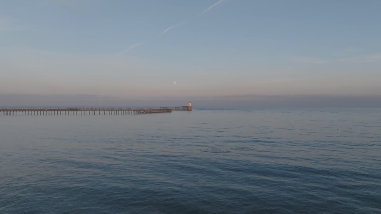 Twilight aerial footage capturing the majestic Blyth Lighthouse under the glowing full moon as Dolphins come up to say hello.