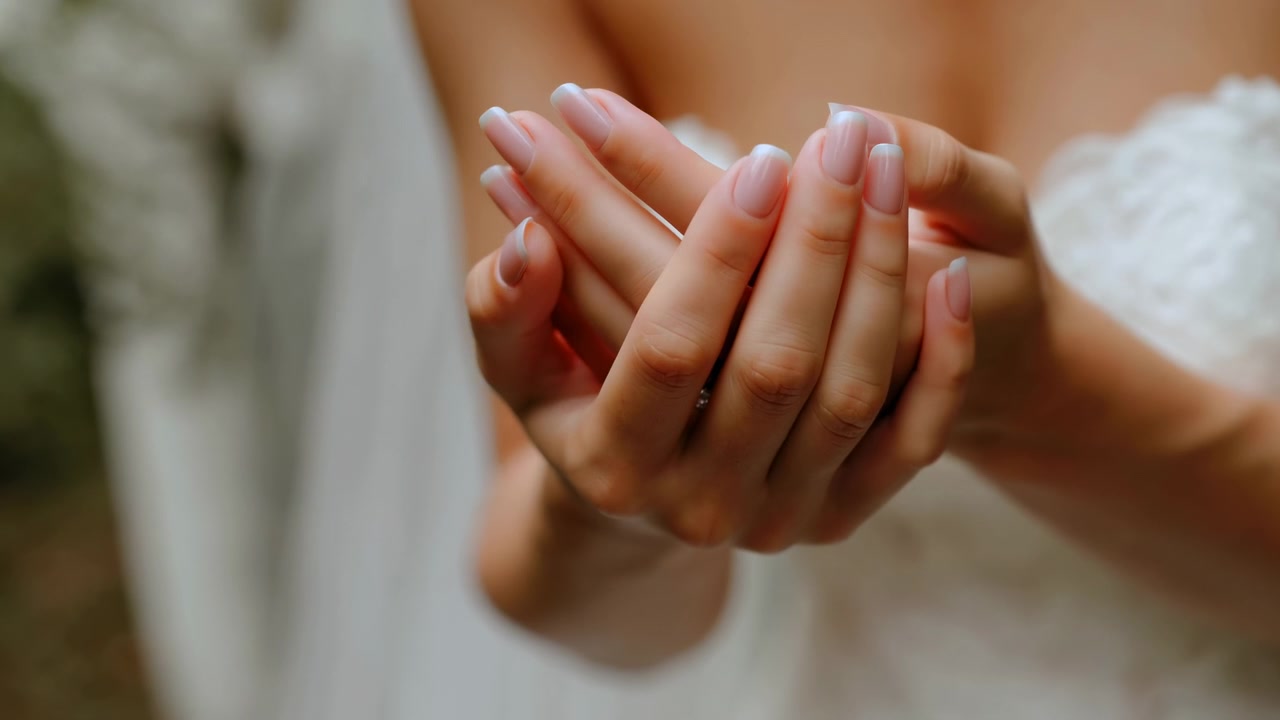 Primer plano de manos caucásicas ahuecadas de novia, vestido de encaje con enfoque suave, bokeh cinematográfico, resplandor de la hora dorada y gesto suave de la palma