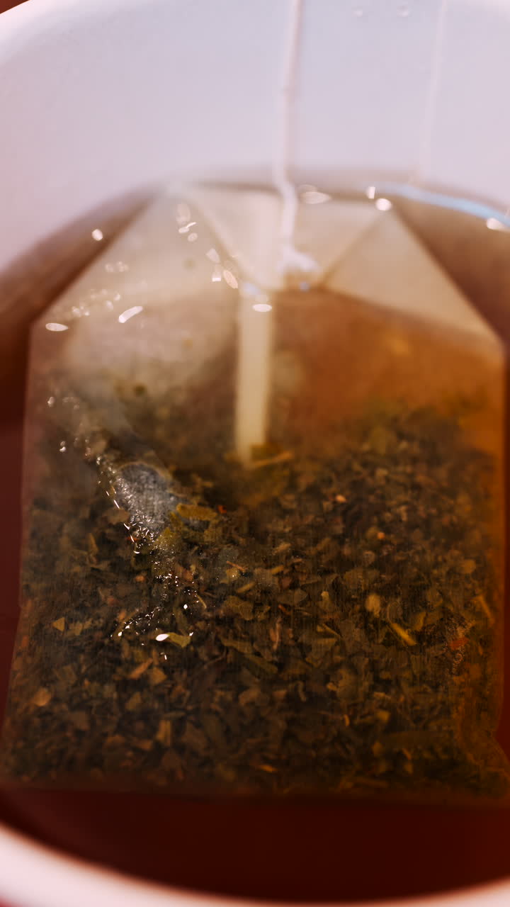 Close up of a tea bag brewing into a red cup. Vertical