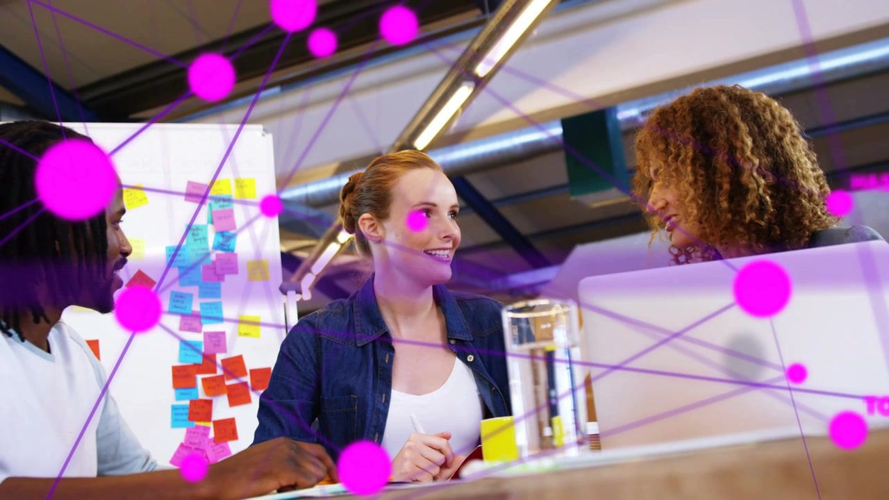 Team working in design office lead woman gesturing as magenta nodes appearing over laptop planning