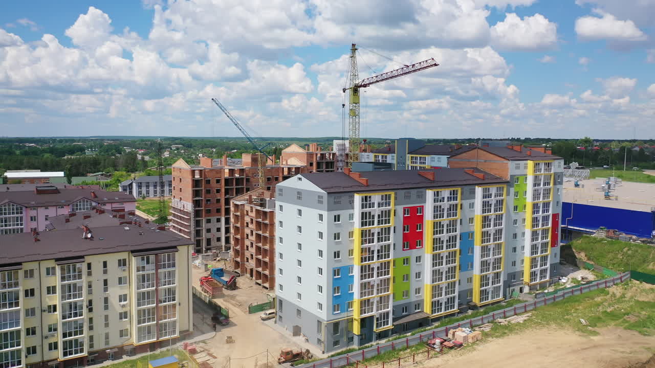 Colorful multi-storey building on a construction site. High rise buildings construction site. Big industrial tower crane with blue sky on background. Aerial drone view. City development.