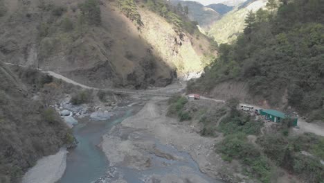 metallic bridge spanning over rocky river bed in mountainous valley surrounded by mountains trees bushes brush rocks dust in kabayan benguet philippines high wide fast aerieal approach