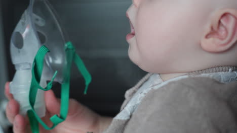 mother holds inhaler mask on 8 month baby and toddler girl breathes the vapor medicine at home