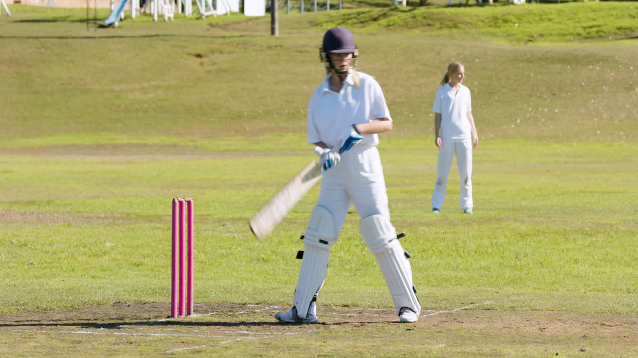 Playing cricket, female batter in protective gear preparing to hit ball