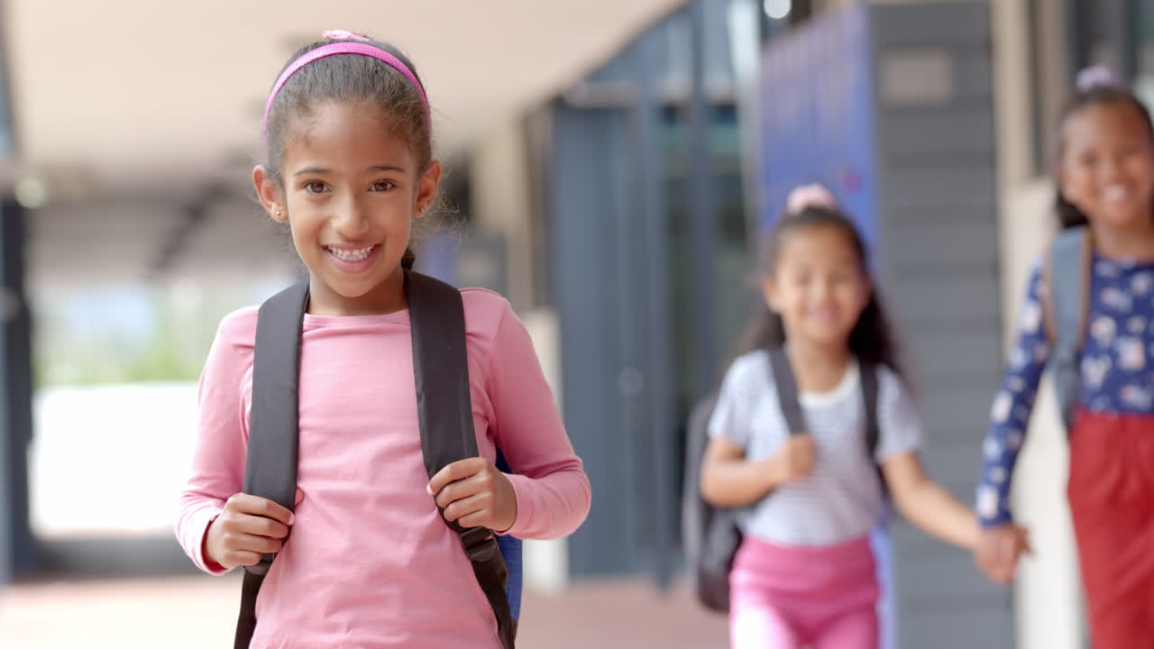 Smiling girl with backpack walking in school hallway with friends in background