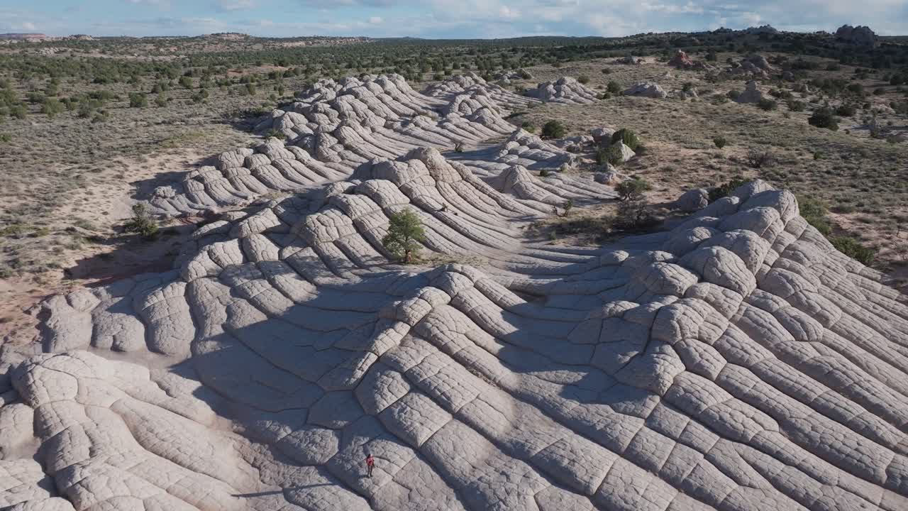 A drone flyover of the unique sandstone rock features of White Pocket Arizona surrounded by sandy desert and blue skies
