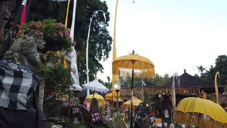 balinese statues, umbrellas and colorful temple decoration displays above blue sky in hindu bali ceremony at samuan tiga landmark, blahbatuh