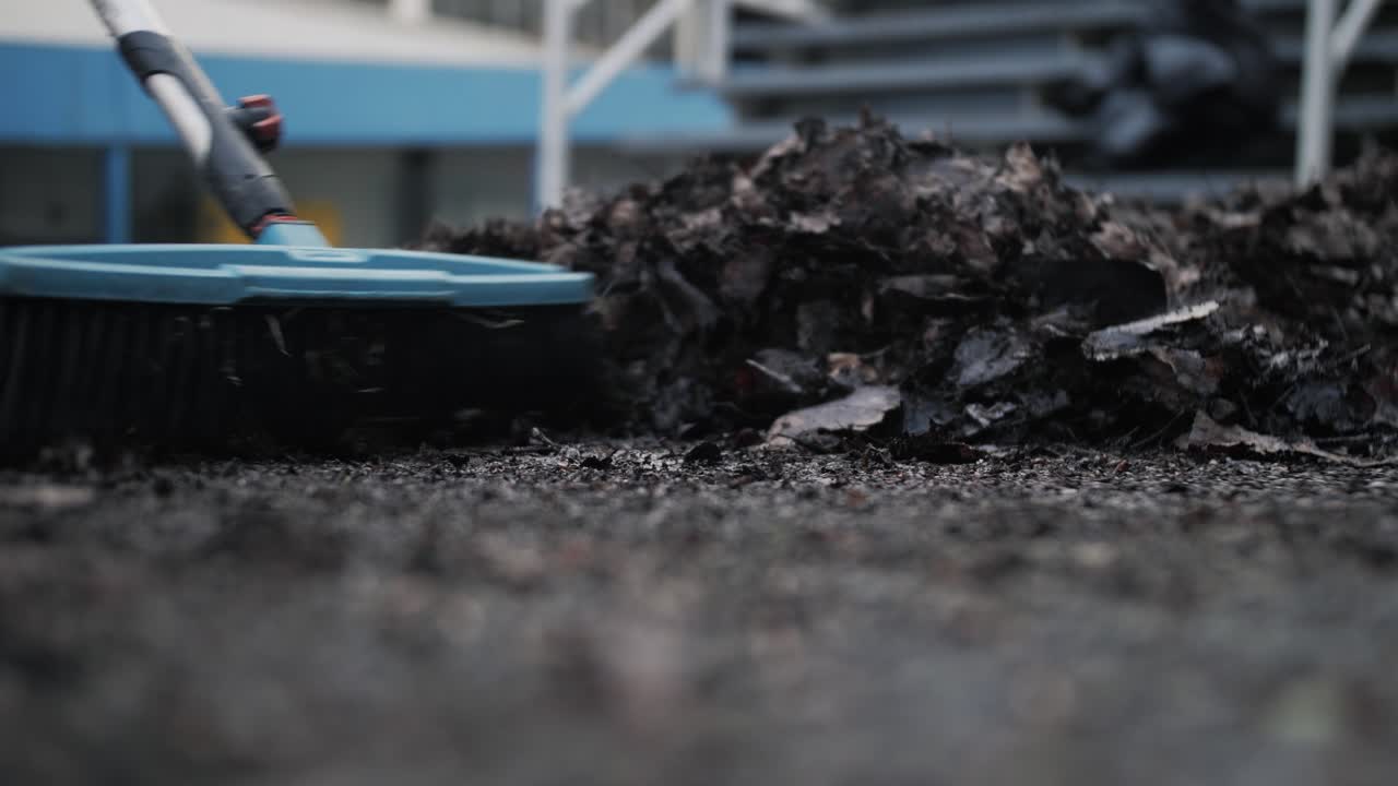 Close-up of a broom sweeping leaves on the ground, showing urban cleaning work in progress