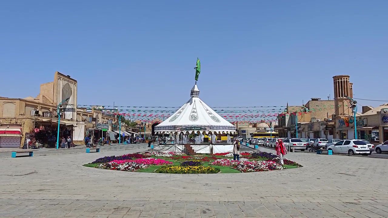 Piazza pubblica con tenda decorativa e aiuola fiorita a Yazd.