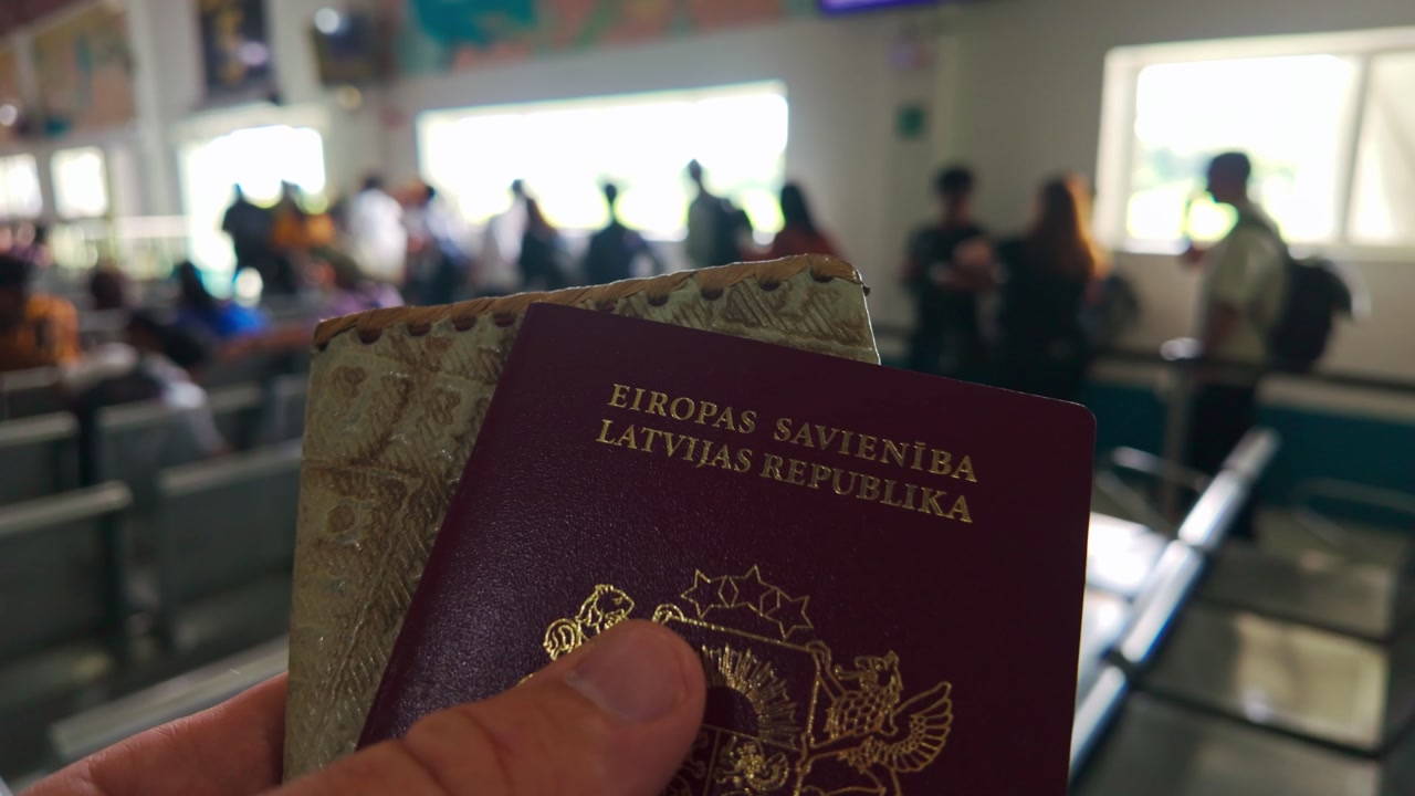 Male traveler shows two Latvian passports while people move in blurred airport