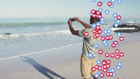 animation of social media icons over african american man taking selfie on beach