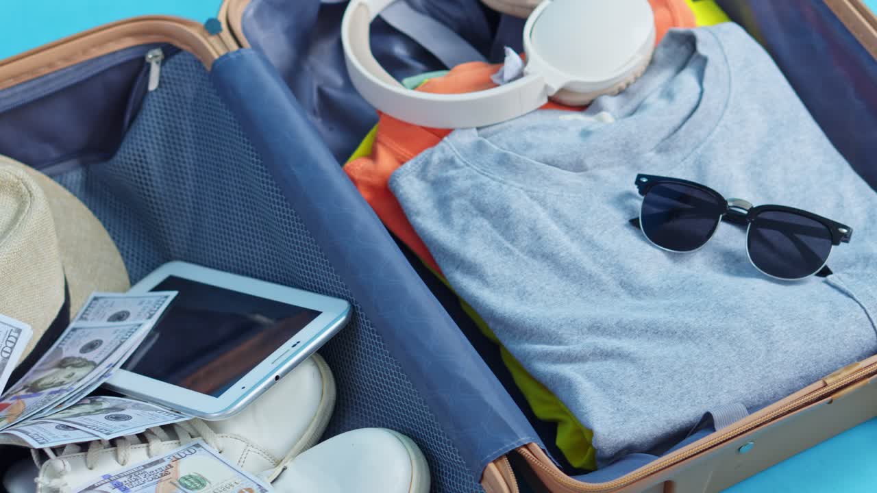 現金、サングラス、夏休みの必需品が入った開いた旅行カバンを真上から見た図。
