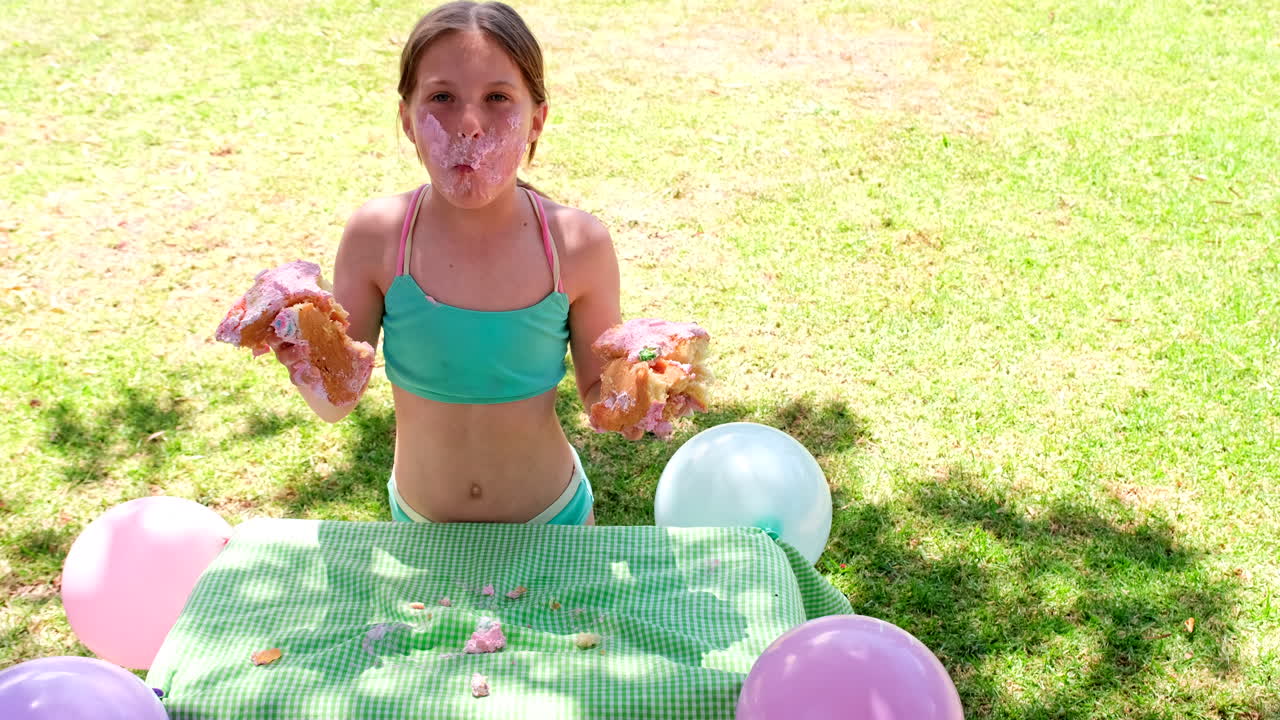 Loony birthday girl eating cake with bare hands on grass outdoors, slomo