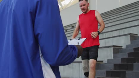 Entrenador-Masculino-Diverso-Y-Atleta-Discapacitado-Con-Entrenamiento-De-Pierna-Protésica,-Corriendo-Escaleras-Abajo