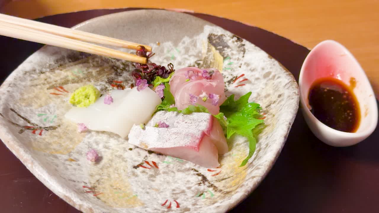 Cận cảnh đũa gắp rau trang trí từ đĩa sashimi tươi ngon kèm nước tương