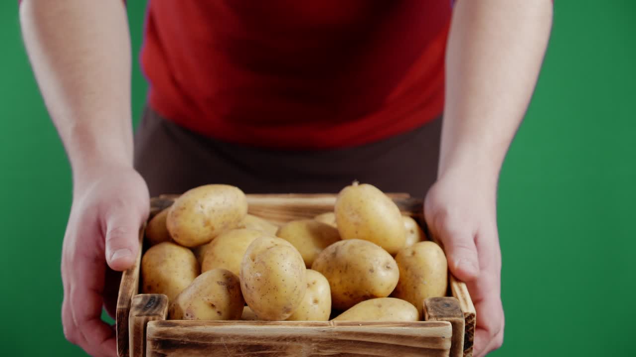 Un uomo tiene una cassa di legno con patate fresche