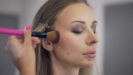 the make-up artist applies the powder on the surface of the young blonde's face