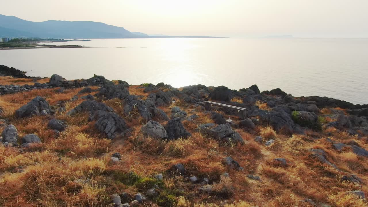 Aerial drone above grass and dirt road towards rocky cliffside and ocean, Greece