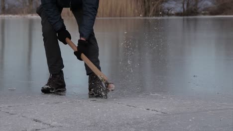 person breaking ice of a frozen lake with an axe