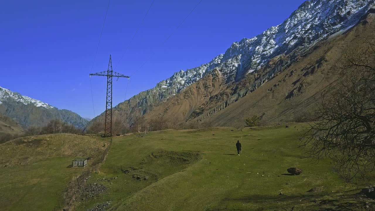 caminante solitario en las montañas con poncho y palo, línea de alto voltaje, árboles, montaña nevada, vista aérea
