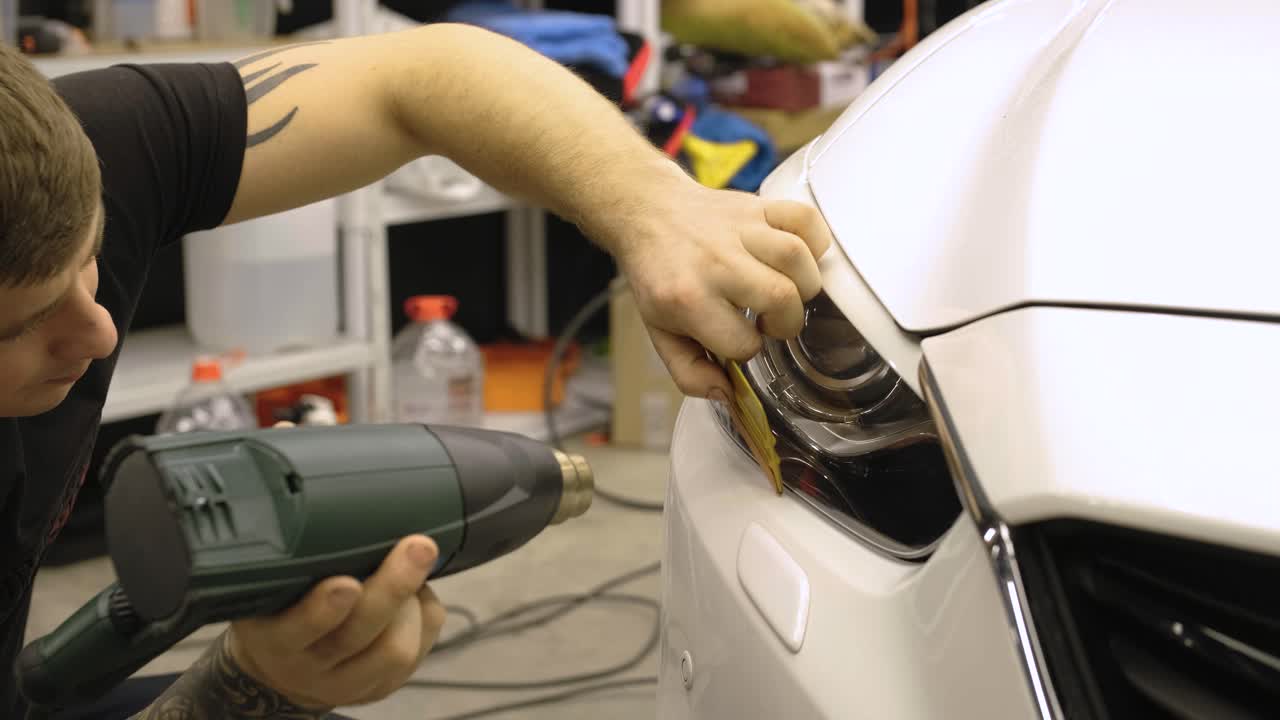 hombre cubriendo el coche con cinta de poliuretano de vinilo. películas para el coche. pegatina película protectora en el faro del coche