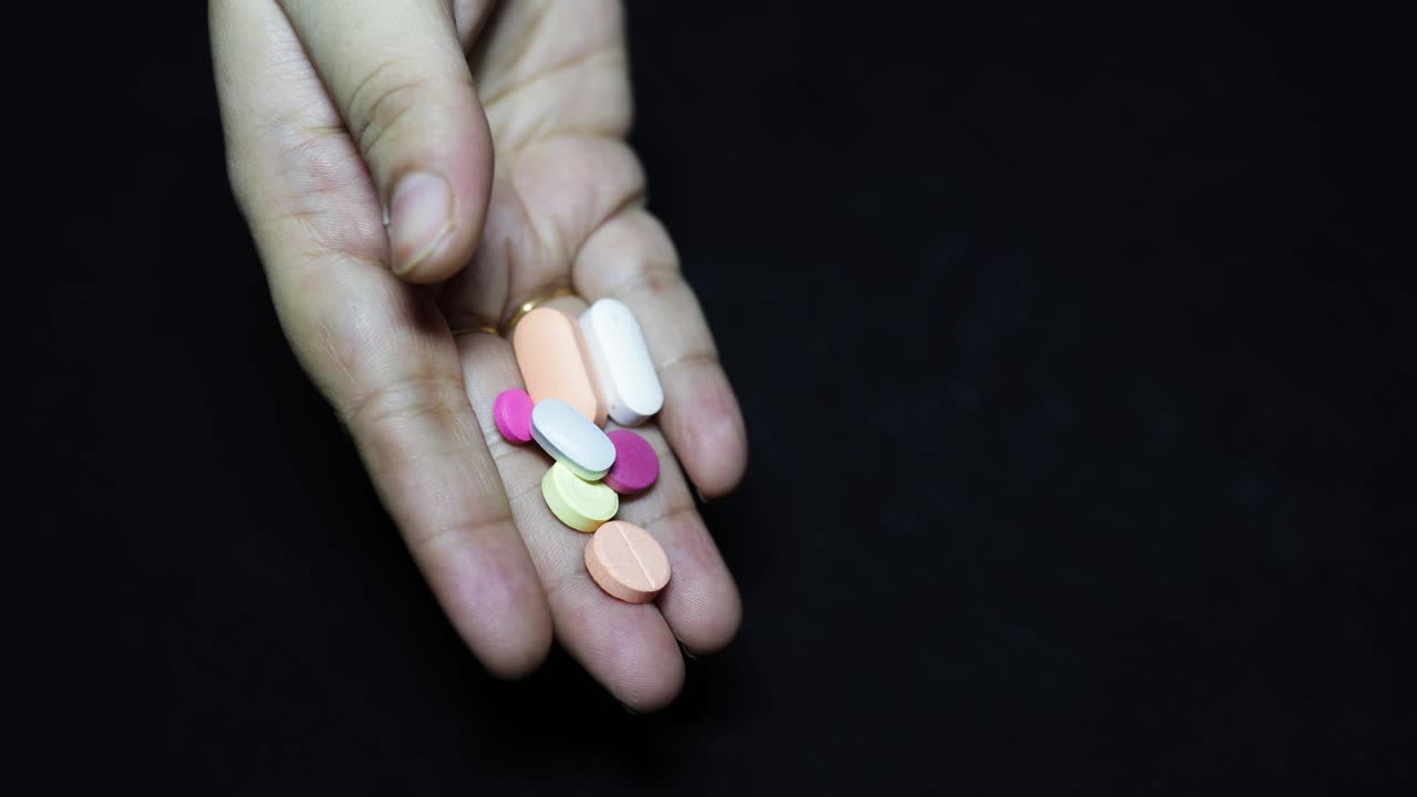 medicine tablets falling from adult palm at black background at indoor