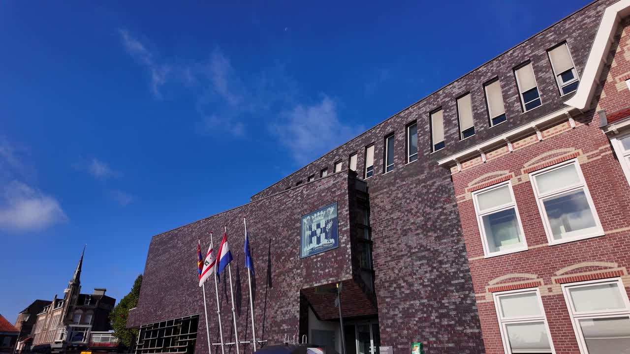 Detailed shot of Coevorden town hall featuring brick architecture, rows of windows, and national flags under bright sunlight. Location: Coevorden, Drenthe, Netherlands (Coevorden, Drenthe, Nederland)